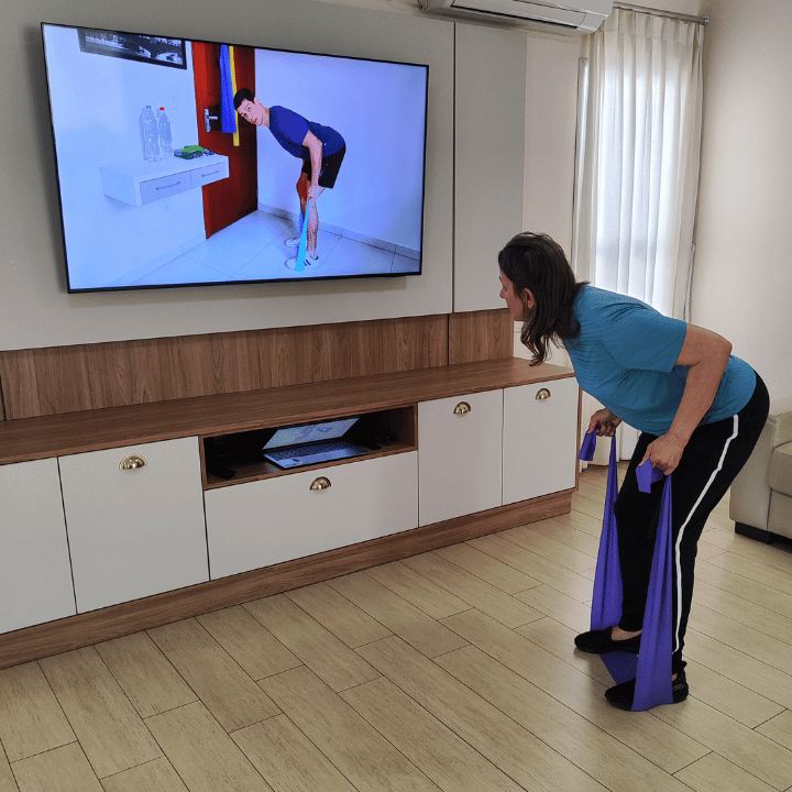 Mulher treinando com elástico em frente à TV