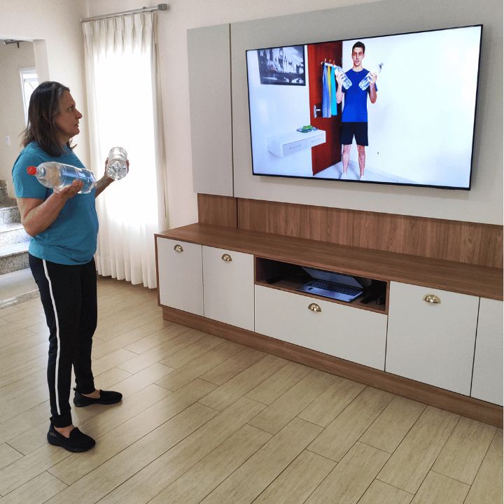 Mulher treinando com garrafas de água em frente à TV