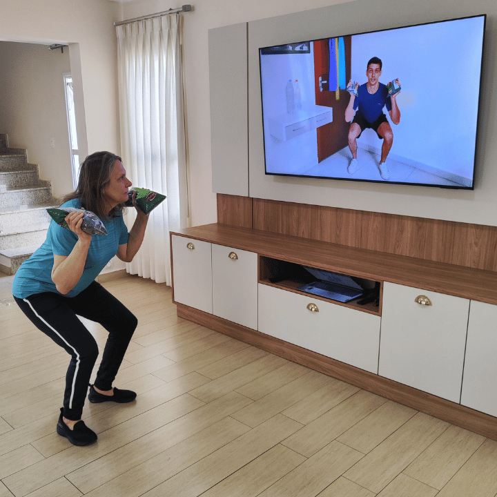 Mulher treinando com pacotes de comida em frente à TV